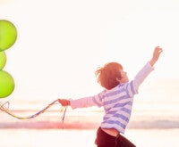 Menino correndo na praia carregando diversos balões coloridos: ter uma criança com epilepsia em casa requer muito carinho e dedicação