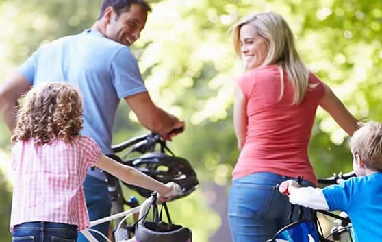 Importância de diagnosticar e tratar a depressão: atividade física. Família reunida em passeio de  bicicleta em em parque. Mãe, pai e crianças alegres e sorridentes. 