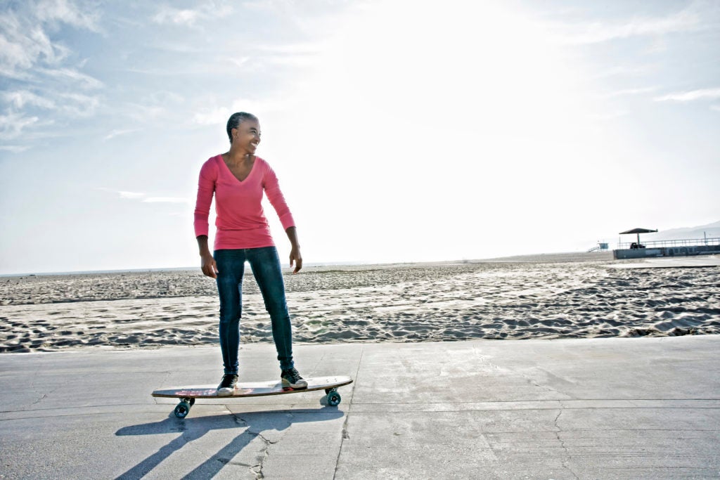 Mulher de meia idade anda de skate na praia em alusão a adotar um estilo de vida saudável no trabalho