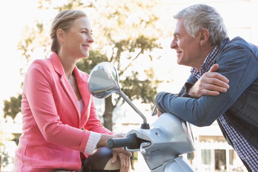 Casal de meia idade conversando em uma scooter sobre quais são os sintomas da menopausa